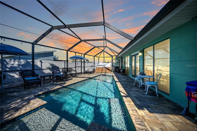 pool at dusk with glass enclosure, a patio area, and a hot tub