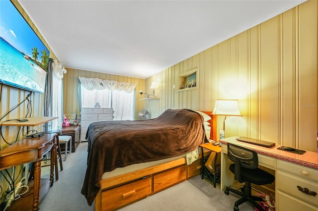 bedroom featuring built in desk, light colored carpet, and wooden walls