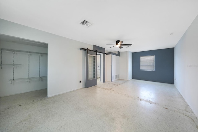 spare room featuring ceiling fan and a barn door