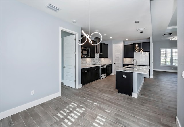 kitchen with a kitchen island with sink, sink, hanging light fixtures, wood-type flooring, and stainless steel appliances