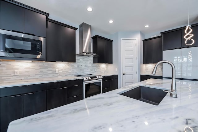 kitchen featuring light stone countertops, appliances with stainless steel finishes, sink, wall chimney range hood, and hanging light fixtures