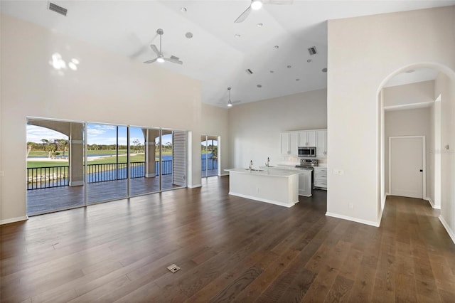 unfurnished living room with high vaulted ceiling, ceiling fan, and dark wood-type flooring