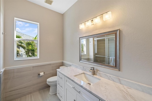 bathroom featuring vanity, tile walls, and toilet