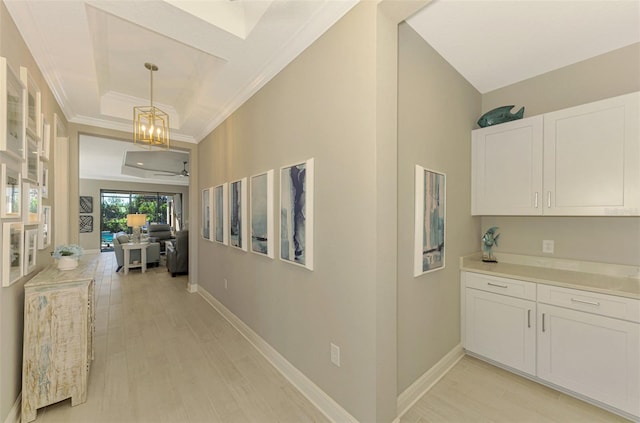 corridor featuring a chandelier, light hardwood / wood-style floors, crown molding, and a tray ceiling