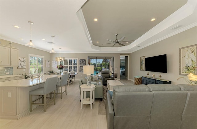 living room featuring a raised ceiling, sink, crown molding, ceiling fan, and light wood-type flooring