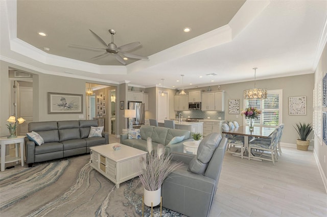 living room featuring a raised ceiling, crown molding, light hardwood / wood-style flooring, and ceiling fan with notable chandelier