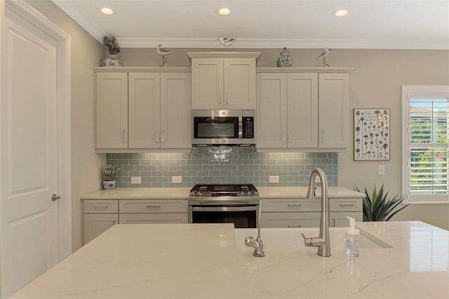 kitchen with light stone counters, white cabinetry, crown molding, and appliances with stainless steel finishes