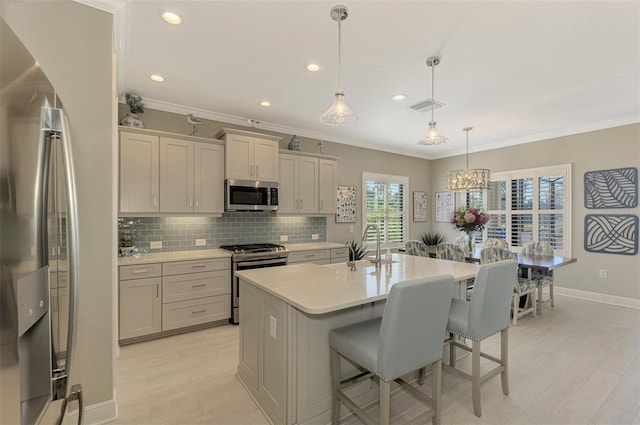 kitchen featuring a center island with sink, crown molding, hanging light fixtures, a kitchen bar, and stainless steel appliances