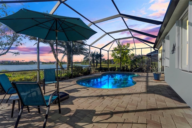 pool at dusk featuring a patio, a water view, and glass enclosure