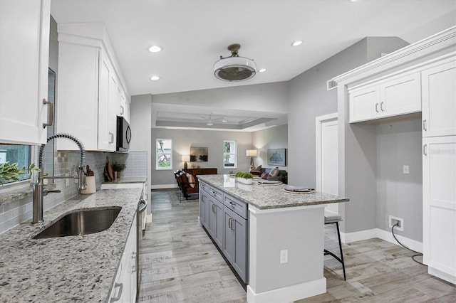 kitchen featuring white cabinetry, sink, light stone countertops, a kitchen breakfast bar, and light hardwood / wood-style floors