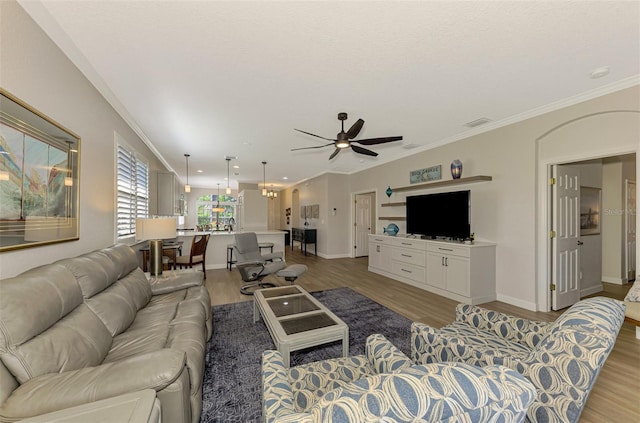 living room with ceiling fan with notable chandelier, ornamental molding, and light hardwood / wood-style flooring