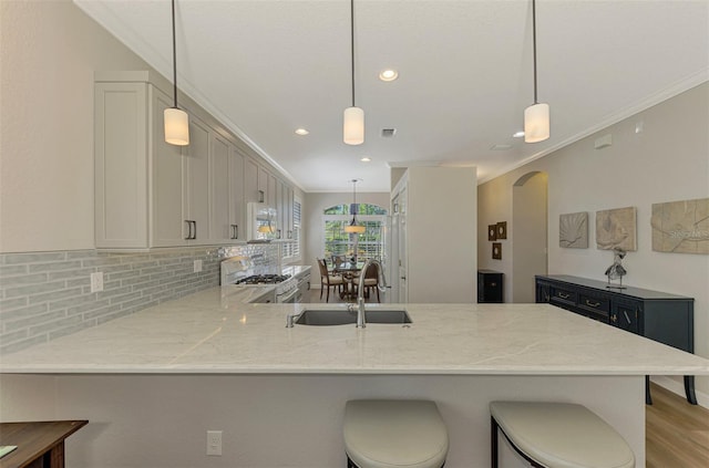 kitchen with kitchen peninsula, backsplash, white appliances, sink, and hanging light fixtures