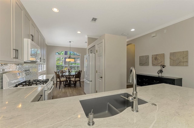 kitchen featuring light stone counters, white appliances, sink, decorative light fixtures, and hardwood / wood-style flooring