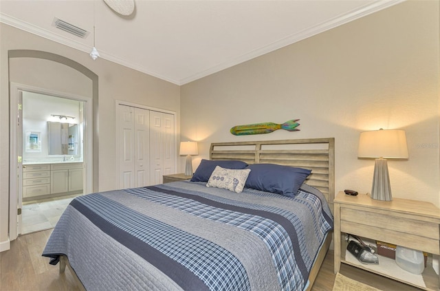 bedroom with wood-type flooring, ensuite bathroom, a closet, and crown molding