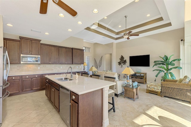 kitchen with sink, tasteful backsplash, a raised ceiling, a kitchen island with sink, and appliances with stainless steel finishes