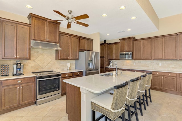 kitchen featuring backsplash, a center island with sink, sink, a kitchen bar, and stainless steel appliances