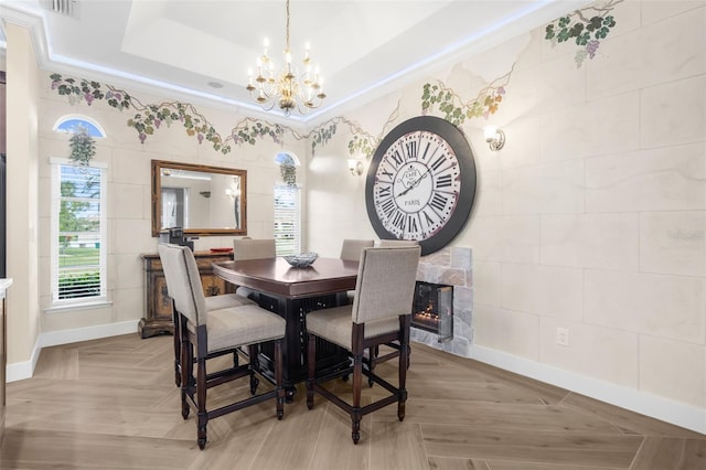 dining area with a chandelier, a tiled fireplace, light parquet flooring, and a tray ceiling