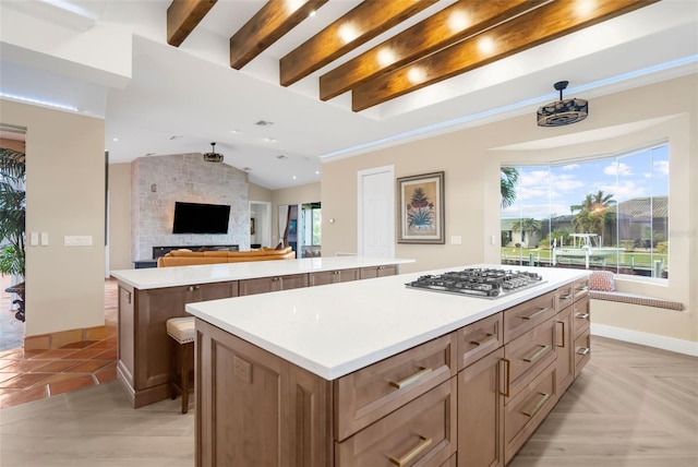 kitchen with a center island, a stone fireplace, vaulted ceiling with beams, stainless steel gas stovetop, and light tile patterned floors