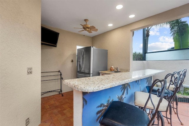 kitchen with a kitchen bar, kitchen peninsula, stainless steel fridge with ice dispenser, and ceiling fan