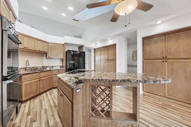 kitchen with dark stone counters, vaulted ceiling with skylight, black appliances, light hardwood / wood-style flooring, and a kitchen island