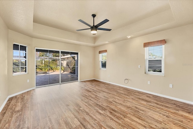 empty room with plenty of natural light, ceiling fan, a raised ceiling, and light hardwood / wood-style flooring