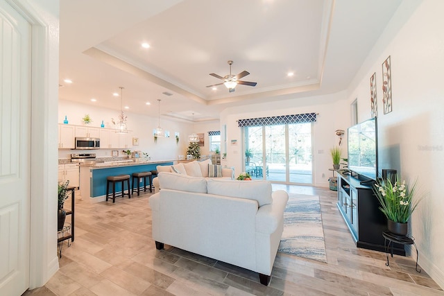 living room featuring a raised ceiling, ceiling fan, and light hardwood / wood-style floors