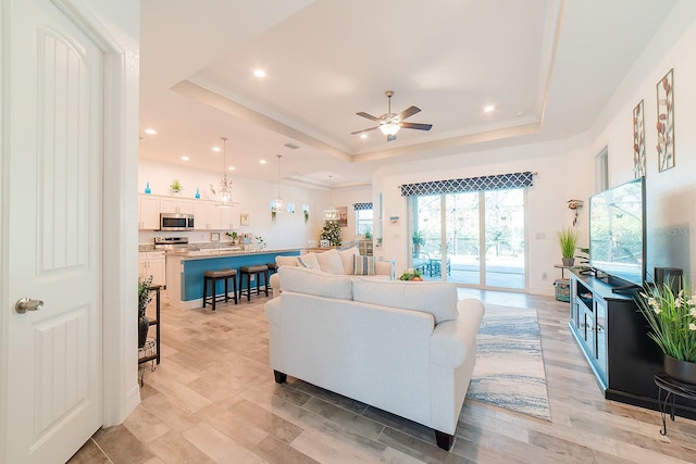 living room with ceiling fan, a raised ceiling, and light hardwood / wood-style flooring