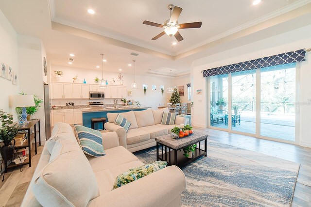 living room featuring ceiling fan, light hardwood / wood-style floors, ornamental molding, and a tray ceiling