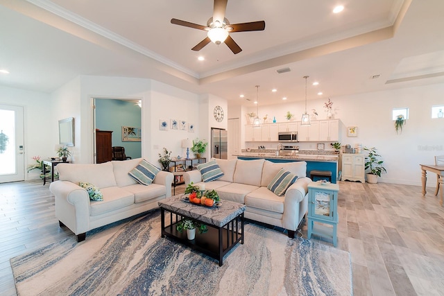 living room with a tray ceiling, crown molding, and light wood-type flooring