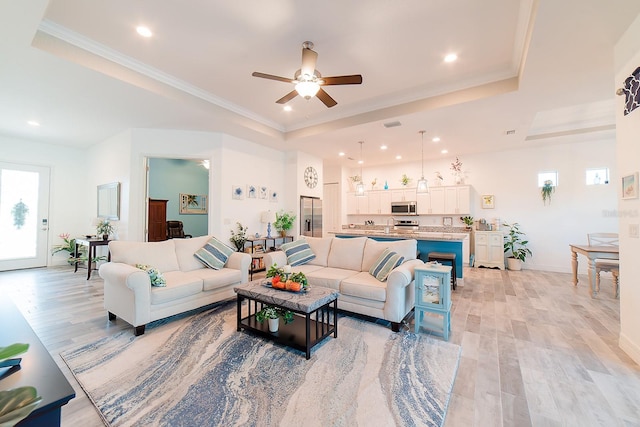 living room featuring ceiling fan, sink, a raised ceiling, crown molding, and light wood-type flooring