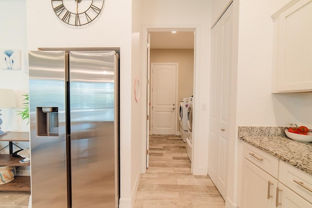 kitchen featuring stainless steel refrigerator with ice dispenser, light stone counters, washing machine and dryer, light hardwood / wood-style floors, and white cabinetry