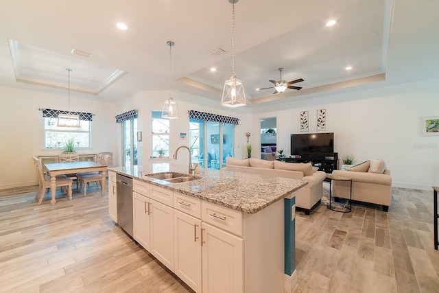 kitchen with dishwasher, a raised ceiling, sink, an island with sink, and white cabinetry