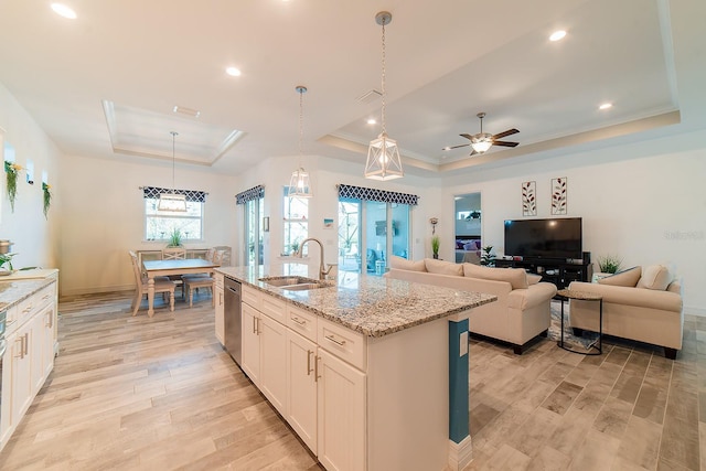 kitchen with a raised ceiling, ceiling fan, decorative light fixtures, white cabinetry, and an island with sink