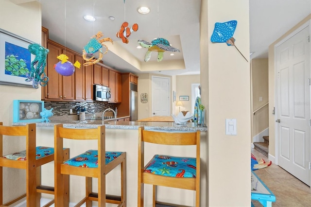 10390 Longshore Rd Unit 82, Placida, FL 33946 - kitchen featuring stainless steel appliances, backsplash, a raised ceiling, light stone countertops, and a peninsula