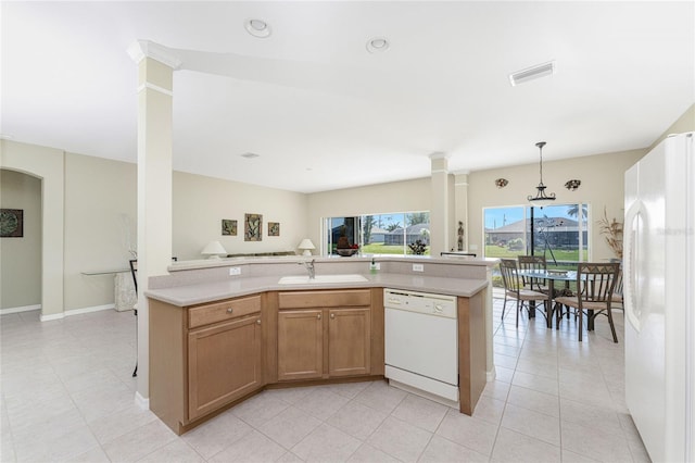 kitchen featuring white appliances, sink, hanging light fixtures, light tile patterned floors, and decorative columns