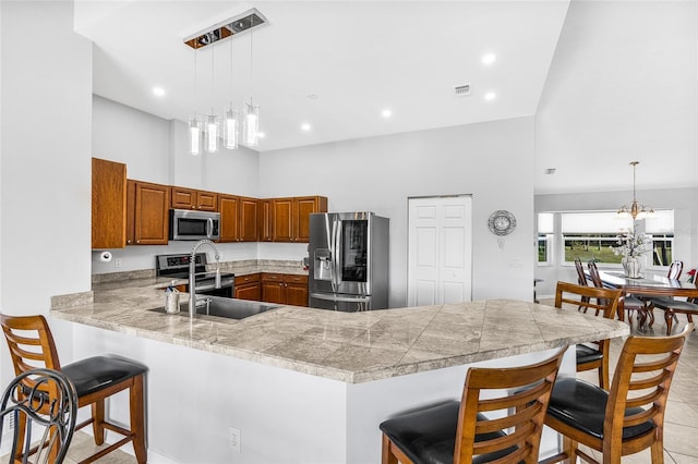 kitchen with kitchen peninsula, a towering ceiling, a chandelier, decorative light fixtures, and appliances with stainless steel finishes