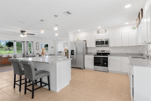 kitchen with stainless steel appliances, ceiling fan, sink, a center island, and white cabinetry