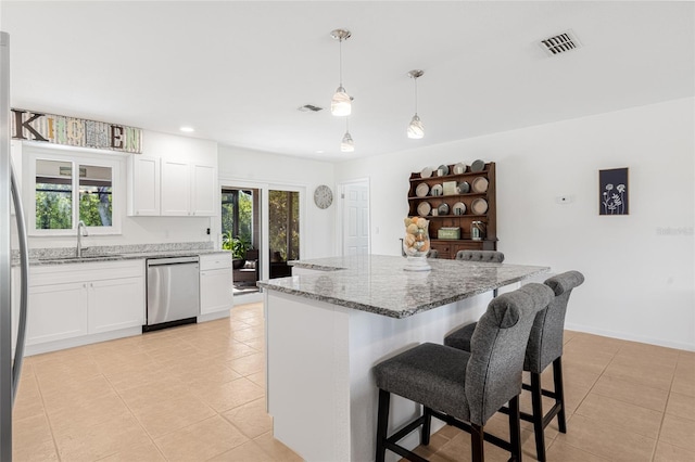 kitchen with a center island, white cabinets, stainless steel dishwasher, decorative light fixtures, and light stone counters