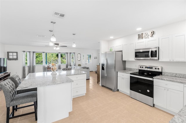 kitchen with a kitchen breakfast bar, stainless steel appliances, white cabinetry, a kitchen island, and hanging light fixtures