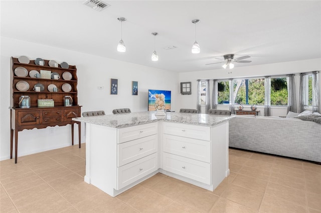 kitchen featuring white cabinets, a kitchen island, ceiling fan, and light stone counters