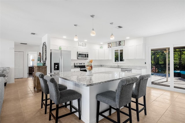 kitchen with a center island, stainless steel appliances, decorative light fixtures, a breakfast bar area, and white cabinets