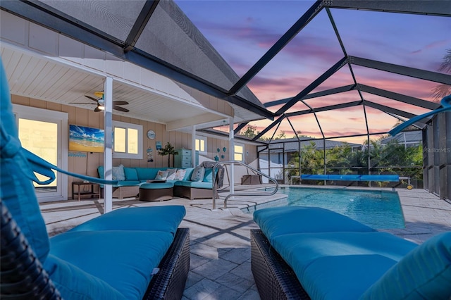 patio terrace at dusk with outdoor lounge area, ceiling fan, a covered pool, a lanai, and pool water feature