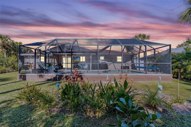 back house at dusk featuring a lanai and a yard