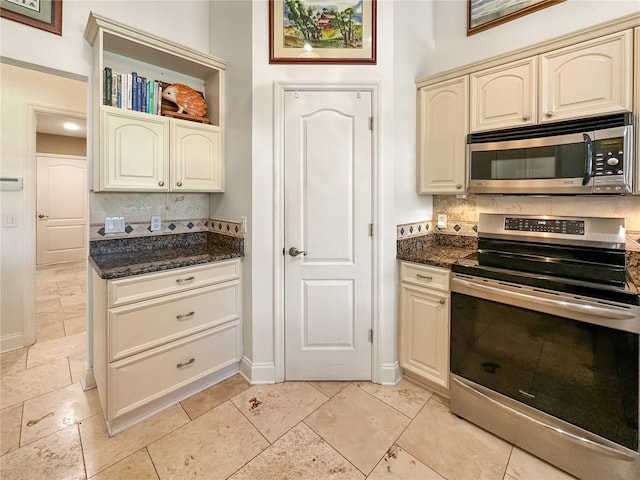 kitchen featuring appliances with stainless steel finishes, dark stone countertops, cream cabinets, and decorative backsplash