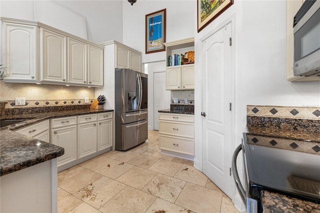 kitchen with a towering ceiling, sink, backsplash, dark stone counters, and stainless steel appliances