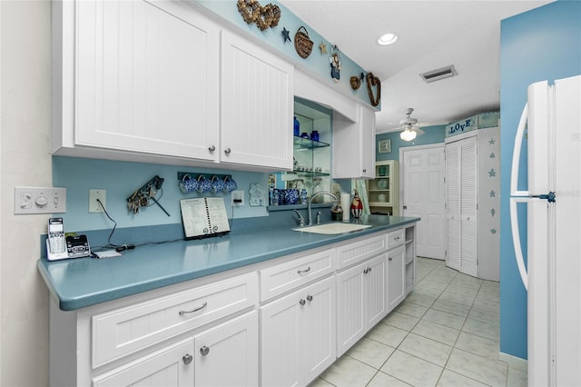 kitchen featuring white refrigerator, sink, ceiling fan, light tile patterned floors, and white cabinetry