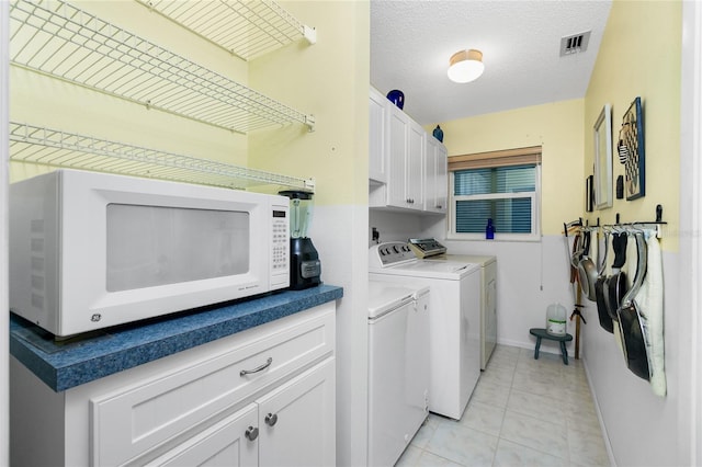 washroom featuring washing machine and dryer, light tile patterned flooring, cabinets, and a textured ceiling