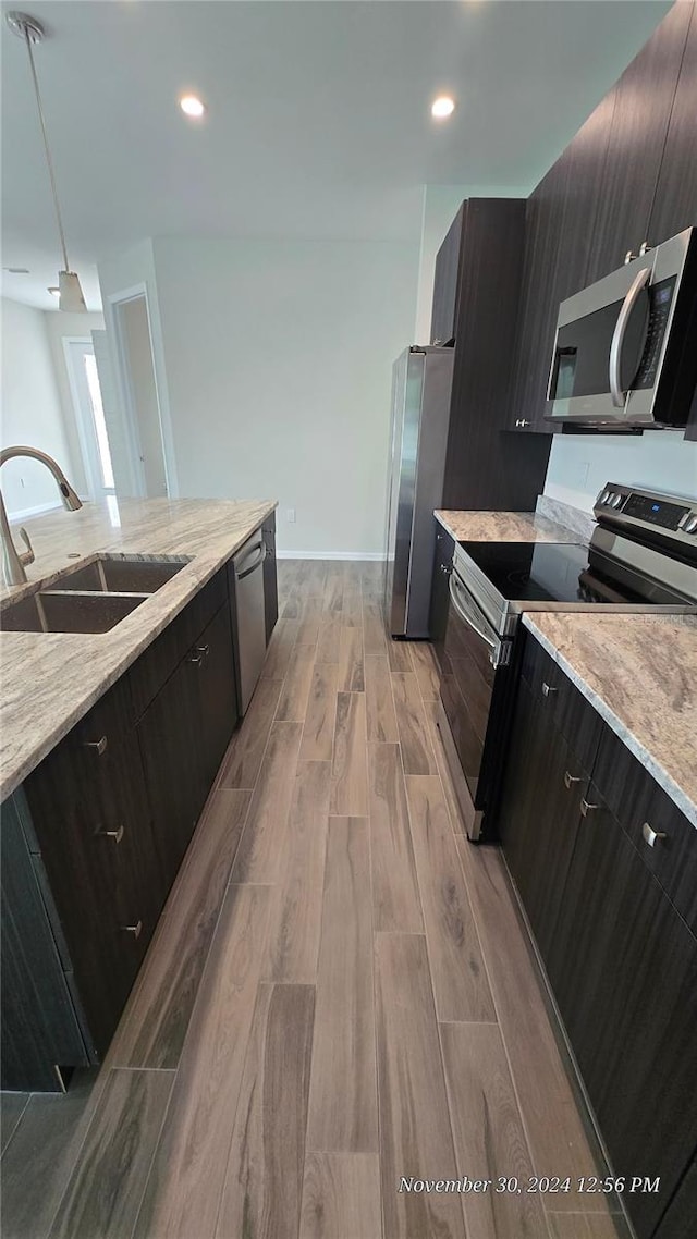 kitchen featuring light stone countertops, stainless steel appliances, sink, decorative light fixtures, and light hardwood / wood-style flooring