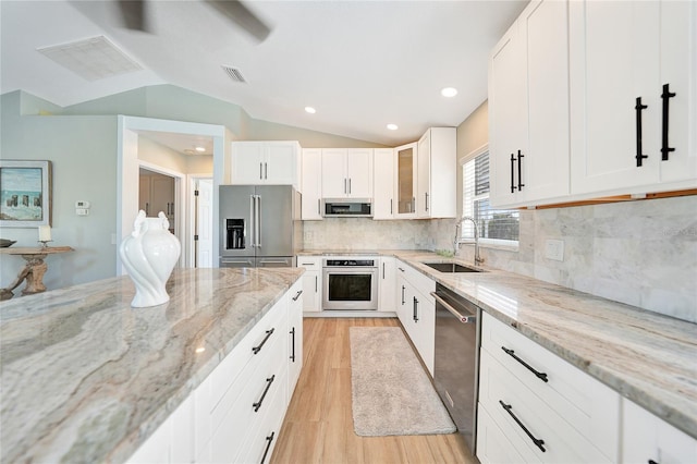 kitchen with light stone counters, white cabinetry, stainless steel appliances, and lofted ceiling