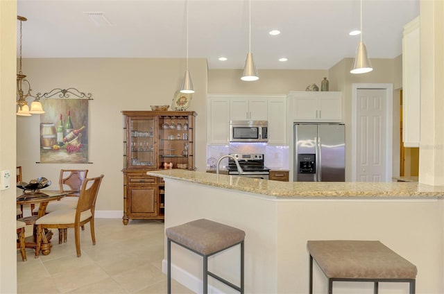 kitchen with kitchen peninsula, appliances with stainless steel finishes, decorative light fixtures, and light stone counters